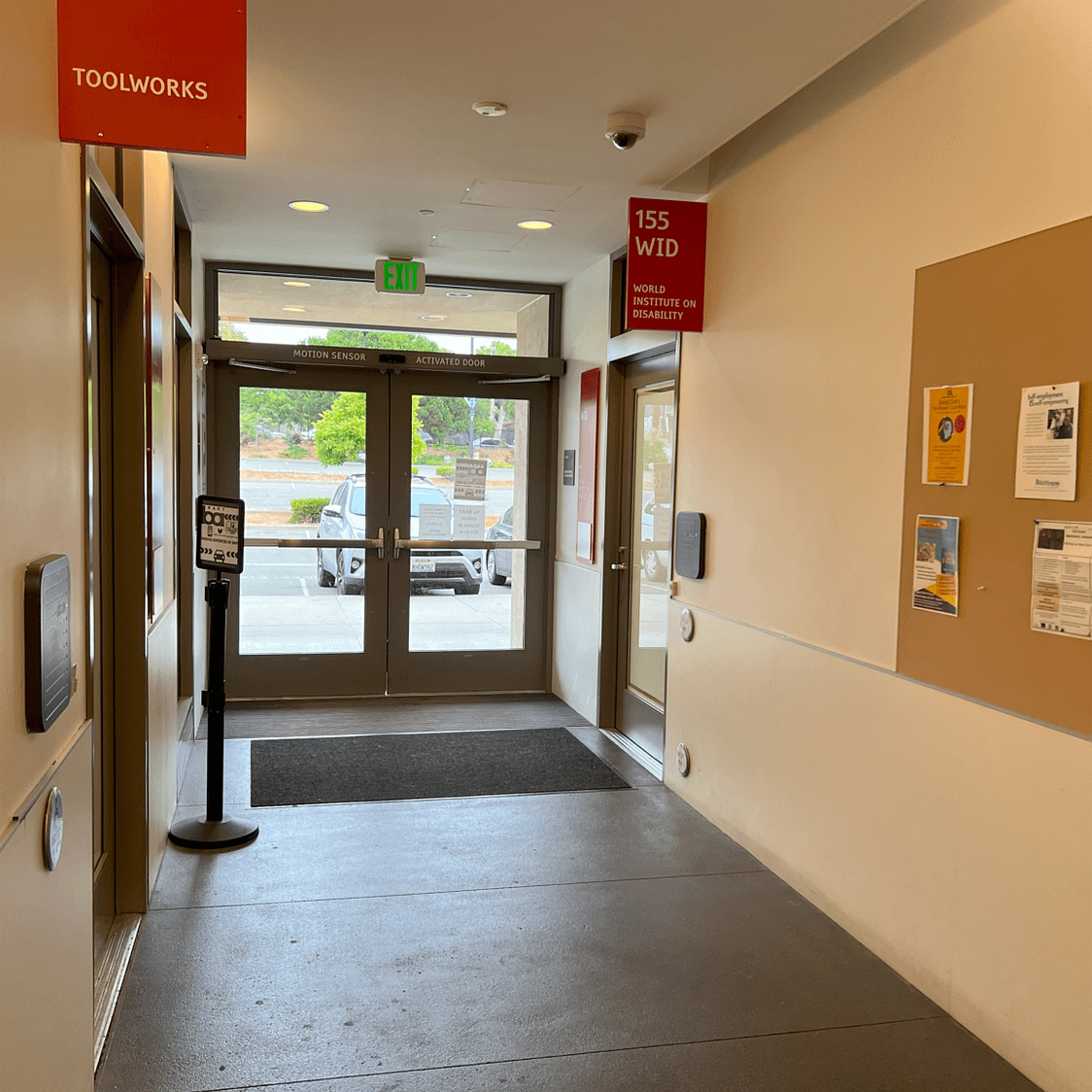 A wide hallway that has doors to World Institutute on Disability, Tool Works, and automatic double doors to exit the building