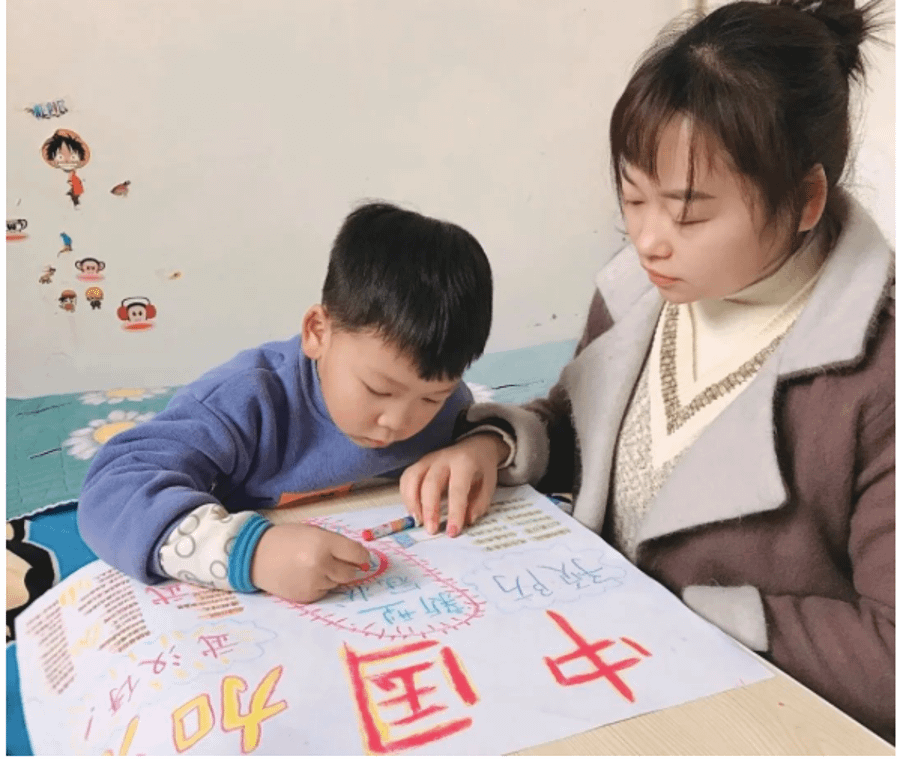 A disabled woman of East Asian descent sitting next to a child coloring and writing with crayons.
