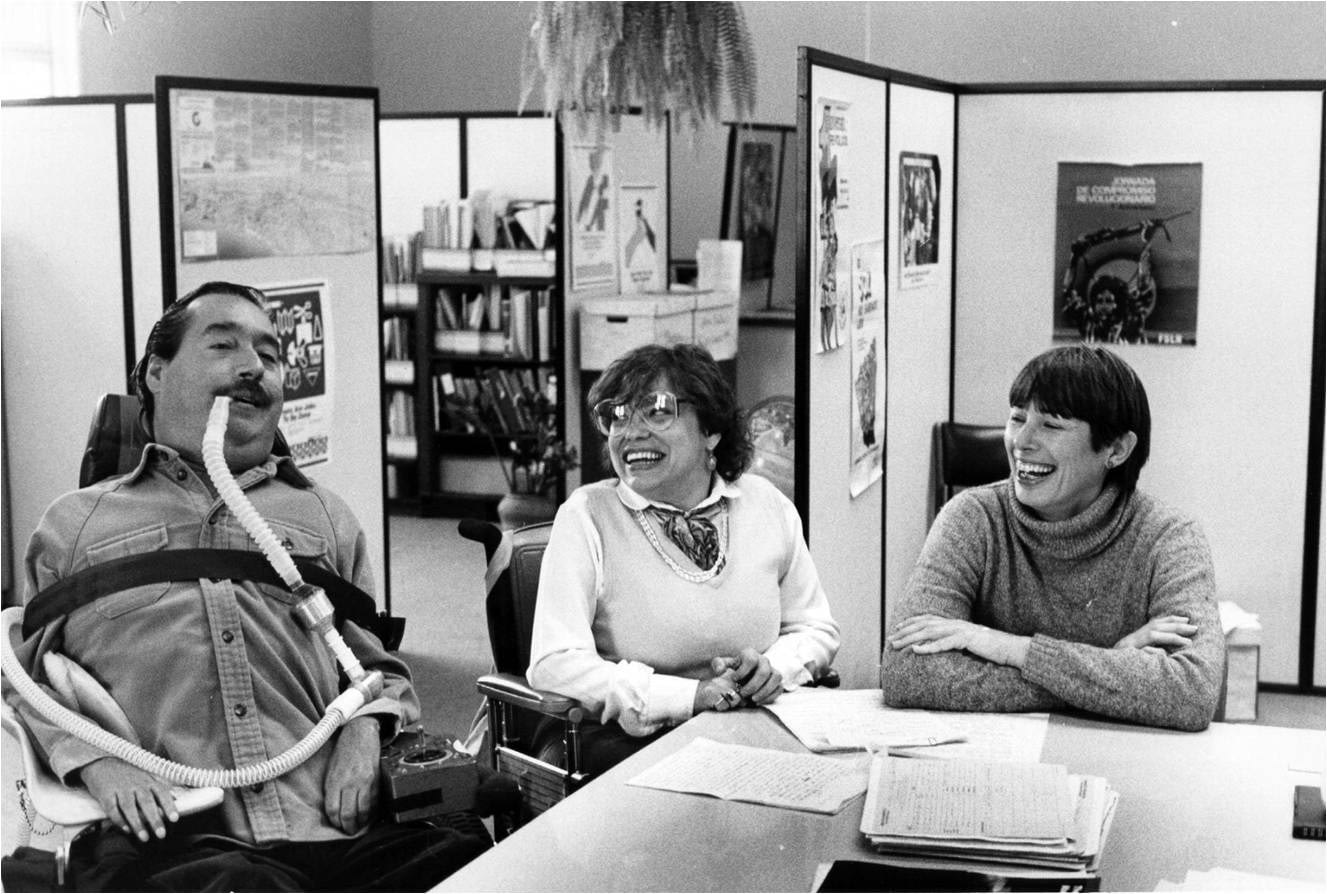 Ed Roberts, Judy Heumann, and Joan Leon talking and laughing in the original WID office