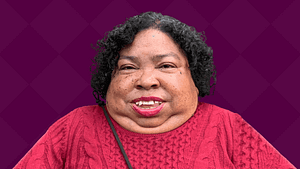 Nikki Brown Booker, a Black and Asian disabled woman with a red sweater smiles.