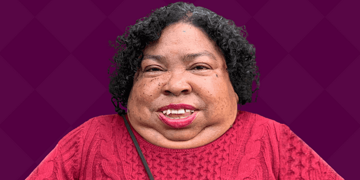 Nikki Brown Booker, a Black and Asian disabled woman with a red sweater smiles.