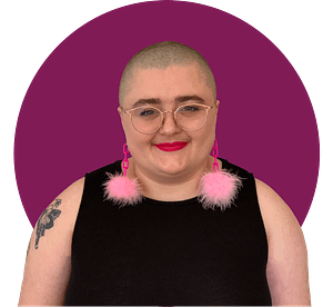 Headshot of Moya, a fat white nonbinary person with a shaved head, wearing pink rimmed glasses.
