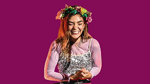 Chloe Hayden smiles with her eyes closed while wearing a flower crown and sparkly dress and long sleeved shirt underneath her dress