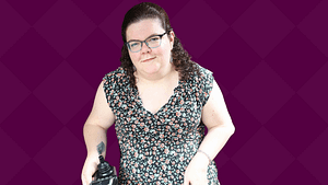 Emily Ladau, a white disabled woman sitting in a wheelchair and patterned gray dress smiles.