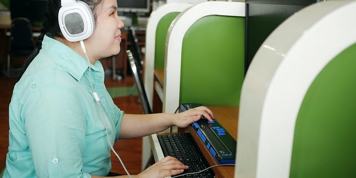 Blind Asian womn using a computer with headphones and a braille display