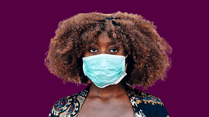 A Black woman with a curly afro wears a face mask.