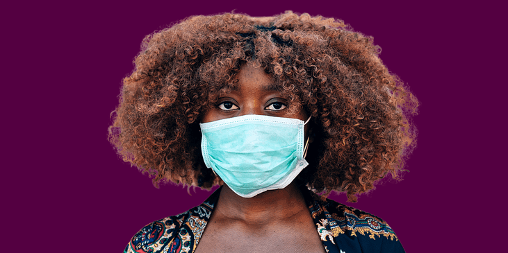 A Black woman with a curly afro wears a face mask.