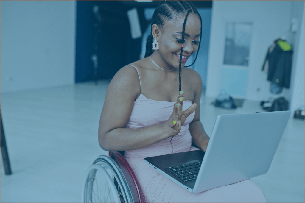 A young, stylish Black woman using a wheelchair smiles and types on her laptop