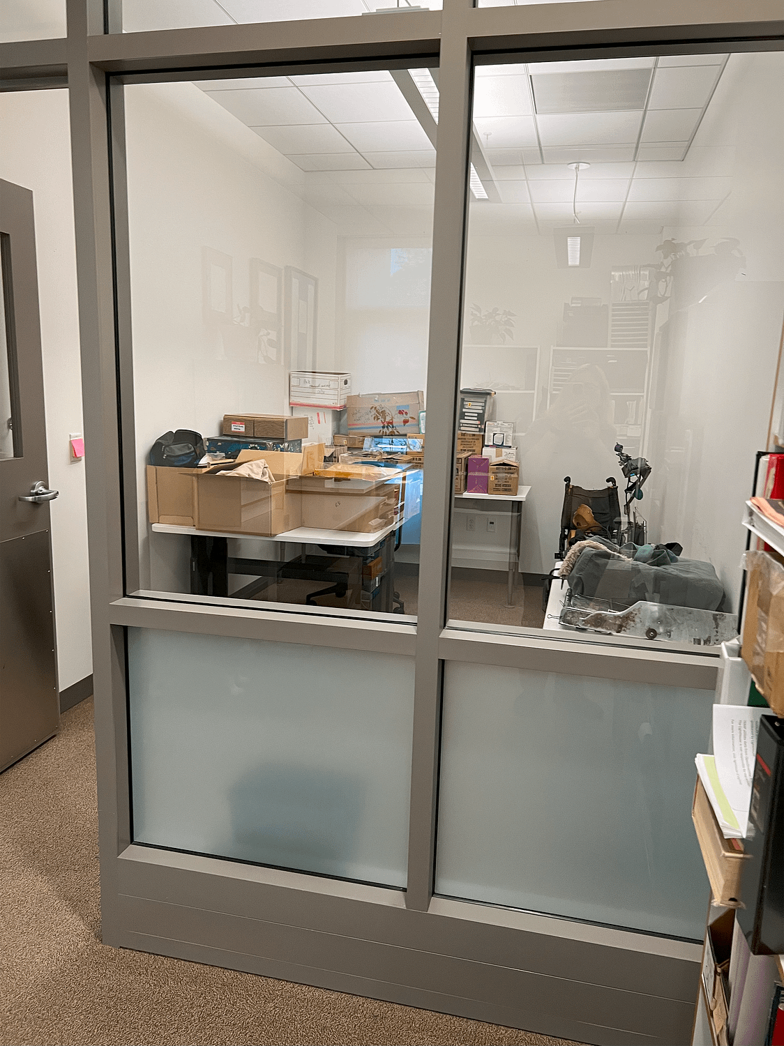 A smaller office with no exterior windows. The room easily fits two large desks and currently holds several packed carboard boxes on the desks, as well as a wheelchair in the corner