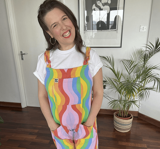 Rosie Jones smiles with her hands in her pockets, wearing rainbow overalls.