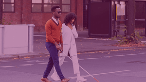 A Black man using a mobility cane and Black woman cross the street