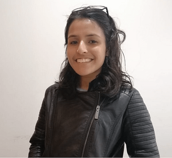 The author, Aishwarya Chouhan, a young Indian woman with shoulder length black hair. She is wearing a black leather jacket and eyeglasses on top of her head. She is smiling.