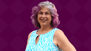 Debra Ruh, a white woman with gray and purple hair and a blue blouse smiles.
