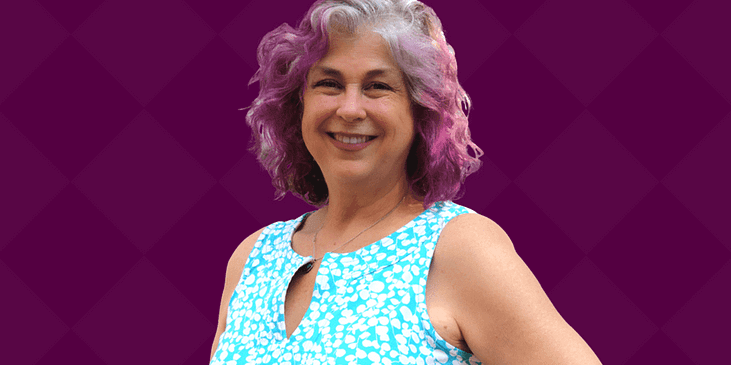 Debra Ruh, a white woman with gray and purple hair and a blue blouse smiles.