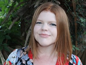 Photo of Karen Fischer, a white person with red hair. She is smiling and wearing a floral print shirt.