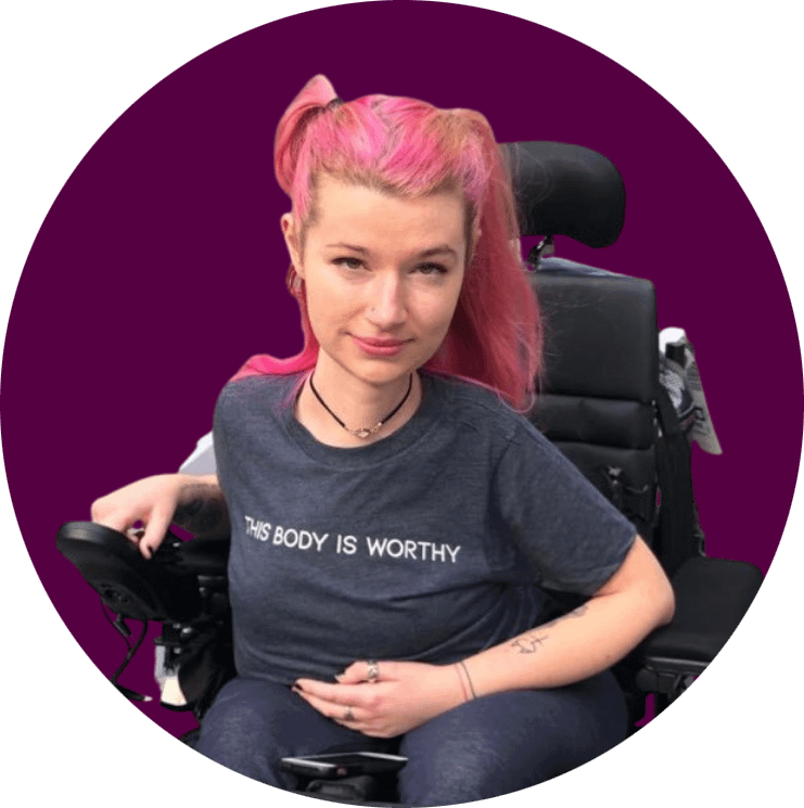 Hannah Soyer, a white woman with pink pigtailed hair sits in her power wheelchair.