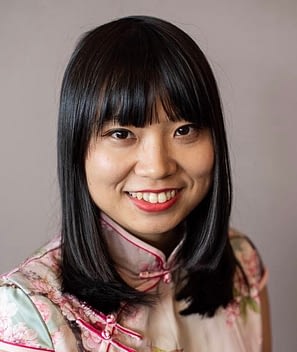 Author photo of LuanJiao Aggie Hu, a Chinese woman with a disability. She is smiling, and wearing a beautiful cheongsam with pink trim.