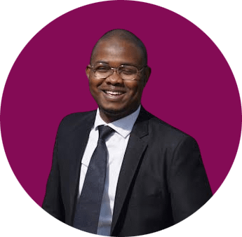 Dikko Yusuf, a Black man wearing eyeglasses and a Black suit and tie, smiles.