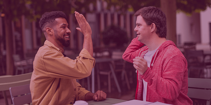 A Black man and a white man with Down’s syndrome high-five one another.