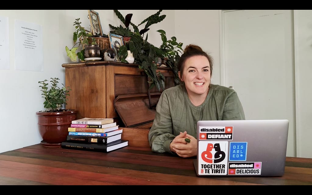 Photo of Robbie Francis Watene sitting at her desk smiling with her laptop in front of her.