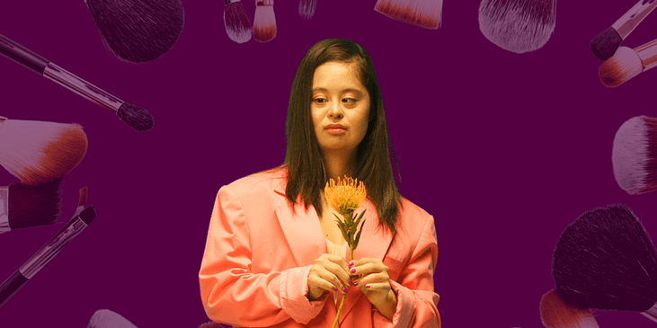 A Woman with Down Syndrome Posing while Holding a Flower. She is surrounded by various makeup paraphanelia