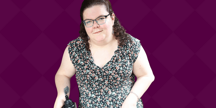 Emily Ladau, a white disabled woman sitting in a wheelchair and patterned gray dress smiles.