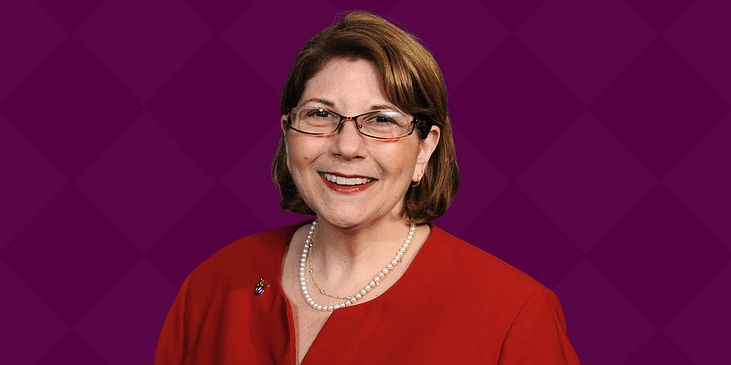 Marcie Roth, a white woman with short brown hair and red dress smiles.