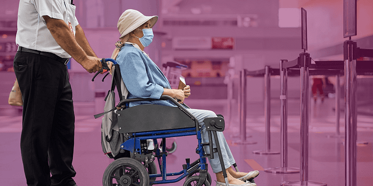 A TSA agent escorts a passenger in a wheelchair into the checkpoint area in an airport.