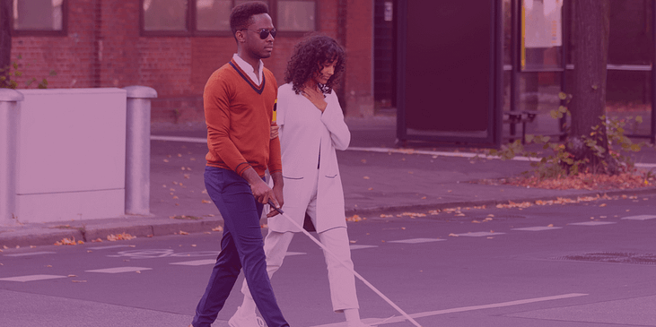 A Black man using a mobility cane and Black woman cross the street
