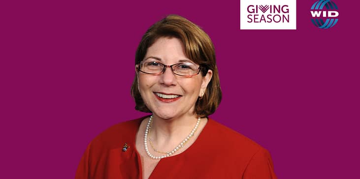 Marcie Roth, a white woman with short hair and eyeglasses smiles while wearing a dress and a pearl necklace. A ‘Giving Season’ logo is also beside Marcie.