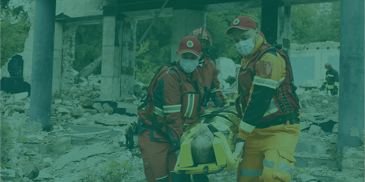 2 rescue workers wearing face masks carry a person out of earthquake rubble.