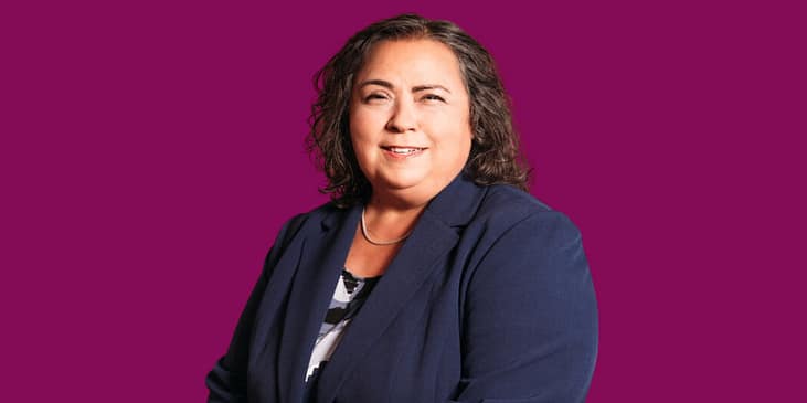 Kathy Martinez, a Hispanic, Brown woman wearing a blazer and blouse smiles.