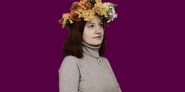 Tanya Herasymova. Beside text is an image of Tanya Herasymova, a white woman with red hair looking to her left while wearing a yellow and orange flower crown and gray turtleneck.
