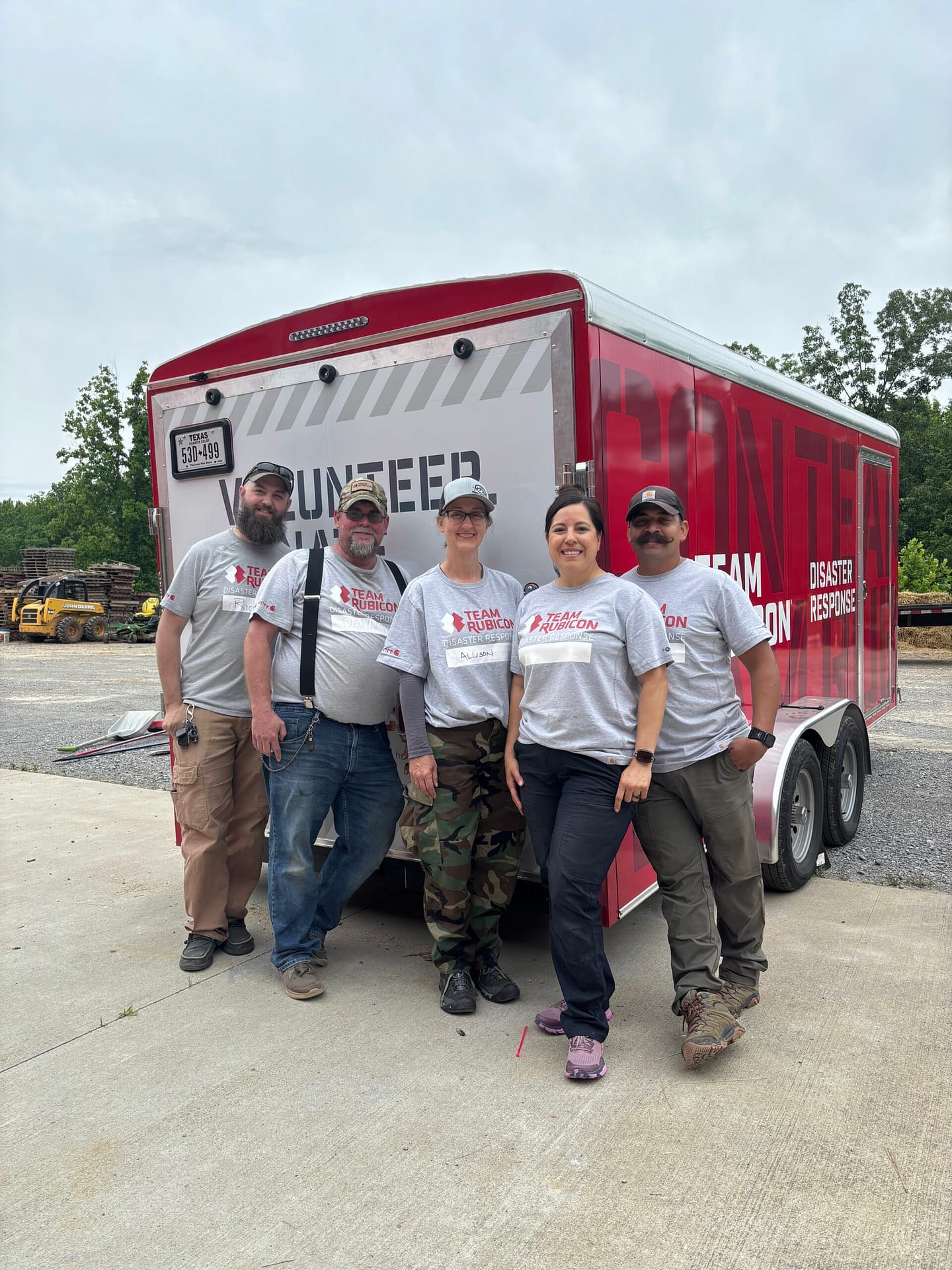 Christina with male and female veterans volunteering with team rubicon in front of a Team Rubicon trailer